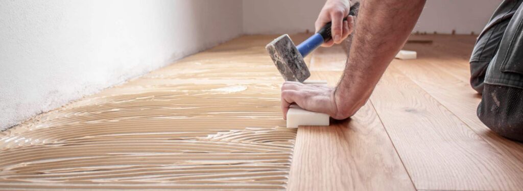 Ein Mann hämmert im Bereich „Über Uns“ mit einem Hammer auf einen Holzboden. T&K WOHNSTDIO - Raumausstattung, Bodenbeläge, Vinylboden, Parkett, Gardinen - Saarburger Straße 25, 67071 Ludwigshafen