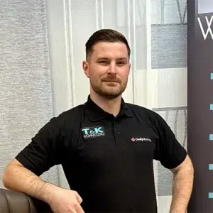 Ein Mann mit kurzen Haaren und Bart steht selbstbewusst da, eine Hand auf der Hüfte. In einem schwarzen Poloshirt von T&K Wohnstudio verkörpert er den „Über Uns“-Spirit und erscheint in einem Büro- oder Showroom-Ambiente, das Professionalität und Stil ausstrahlt. - T&K WOHNSTDIO - Raumausstattung, Bodenbeläge, Vinylboden, Parkett, Gardinen - Saarburger Straße 25, 67071 Ludwigshafen